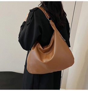 Nahaufnahme der karamellbraunen Schultertasche mit Ösen am Trageriemen und schwarzem Mantel