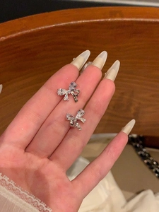 Detailed view of silver bow earrings with shimmering zircon stones held by hand