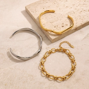 Three-piece stainless steel bracelet set with wave bangles on beige stone pedestal