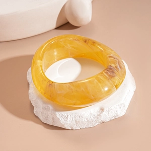 Close-up of a wide yellow resin bangle with amber marble texture on a stone stand