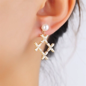 Close-up of model wearing long gold pearl earrings with geometric zircon details