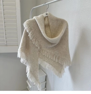 Detailed close-up of beige knitted wool shawl featuring soft tassels on a white hanger