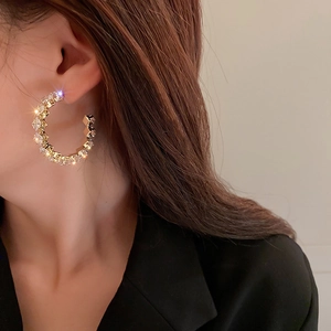 Close-up of sparkling gold C-shaped hoop earrings with zircons on model ear