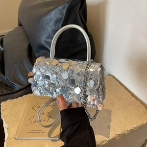 Detail shot of silver sequin handbag with metal chain strap and top handle held by hand