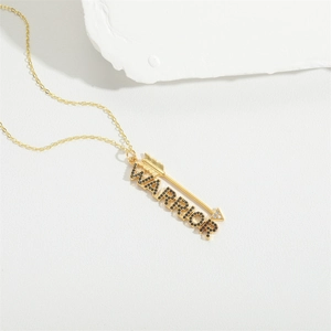 Golden and black Warrior letter necklace with arrow pendant on white stone surface