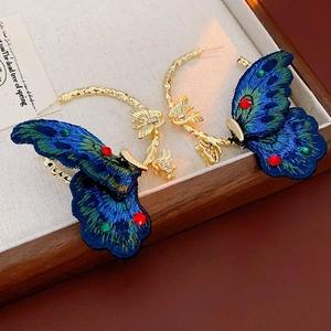 Dettaglio di orecchini a farfalla in tessuto con ricamo blu e strass colorati