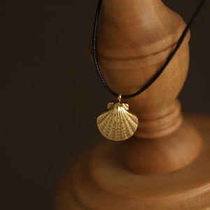 Ocean-inspired gold shell pendant necklace with black cord cord on a wooden stand