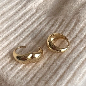 Close-up of minimalist gold polished hoop earrings on beige knit sweater background