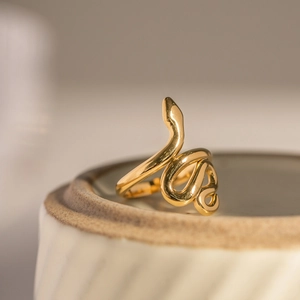 Detail of golden snake-shaped open ring on ceramic base with high-gloss metallic finish