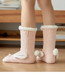 Detail of pink knitted rabbit slipper socks with white plush ears and fluffy pom-pom tail