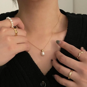 Close-up of a delicate gold pearl necklace with layered rings on a fashion model