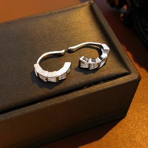 Detailed macro view of silver snake-shaped ear cuffs with cubic zirconia on black leather