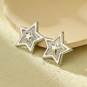 Detailed view of silver hollow star earrings with geometric layered design on beige tray