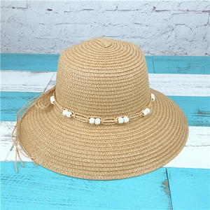 Detail of hand-woven straw sun hat featuring elegant white bead accents and a wide brim