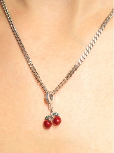 Macro shot of red cherry pendant necklace with green crystal leaves on a silver chain
