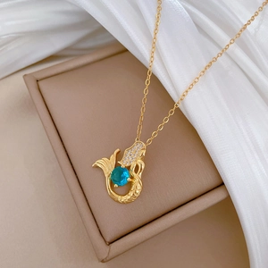 Detailed close-up of a gold mermaid pendant with blue sapphire and crystals on silk fabric