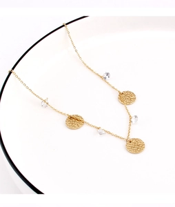 Detail of golden chain necklace with hammered metal discs and faceted crystals on a ceramic tray