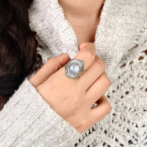 Détail d'une bague vintage en pierre de lune avec texture argentée sur pull blanc