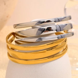 Gros plan de bracelets joncs empilés en or et argent sur un socle blanc épuré