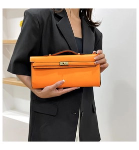 Detail of vibrant orange PU leather handbag with metal turn-lock closure on black suit