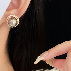 Close-up of golden hollow earring with grey pearl and shimmering micro-set zircons
