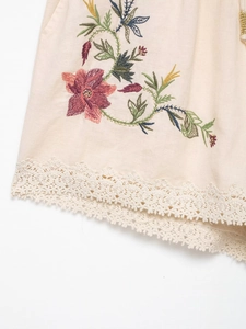 Detailed macro view of multi-color floral embroidery and lace trim on linen-cotton shorts