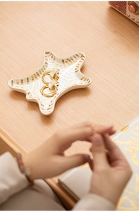 Star-shaped ceramic jewelry tray with gold stripes and gold earrings on wood surface