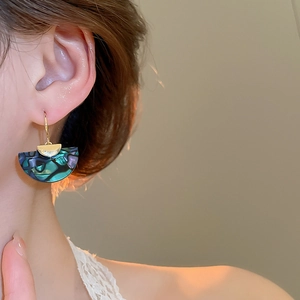 Detail of abalone shell fan earrings with green resin and gold hook on model