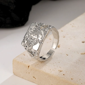Detail shot of irregular lava texture on a silver wide band ring placed on a beige stone