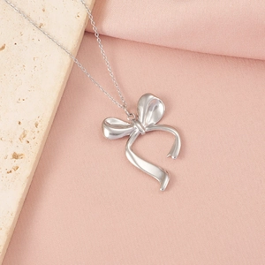 Gros plan du pendentif nœud en argent poli sur tissu rose et surface de marbre