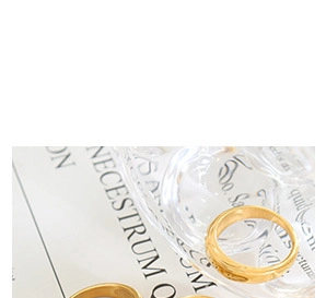 Minimalist gold hollow C-shape earrings on glass prop with vintage paper aesthetic