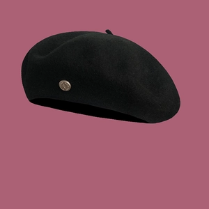 Detail of a black wool beret featuring a classic circular metal crest on a pink backdrop