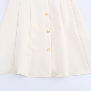 Close-up of pleated cream-colored skirt with three elegant golden decorative buttons