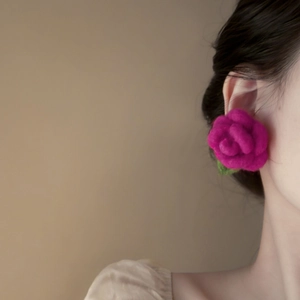 Close-up of a large magenta flocked rose earring with green leaves worn by a model