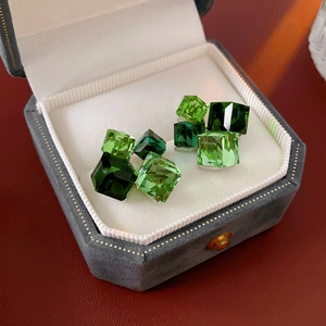 Macro detail of cube-cut green crystal earrings in a grey velvet jewelry gift box