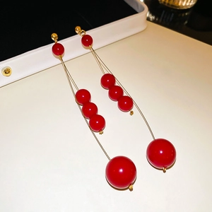 Close-up of red pearl drop earrings with gold wire gradient design on white background