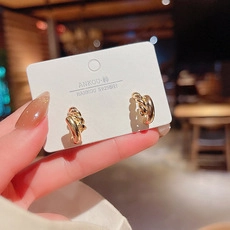 Primer plano de pendientes de aro dorados trenzados con detalle de aguja de plata S925