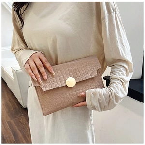 Detail of beige envelope clutch bag featuring crocodile texture and gold metal ring buckle