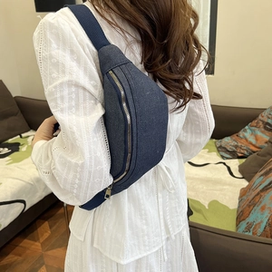 Women's dark blue denim canvas waist bag with gold zipper shown on model indoors