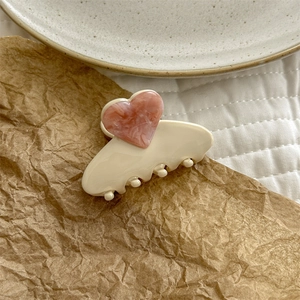Detail view of heart-shaped marble acetate hair claw clip on cream base