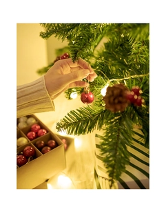 Close-up of 3cm red Christmas tree ball ornament being hung on a festive warm tree
