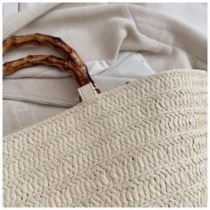 Close-up of beige woven straw tote bag featuring a polished bamboo top handle detail