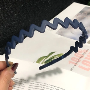 Detail of dark blue wavy plastic headband with anti-slip teeth held over a magazine