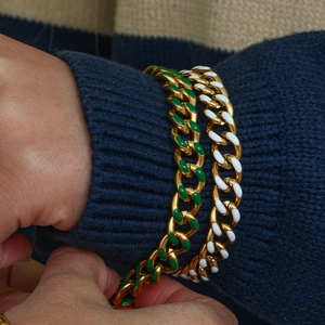 Detail of chunky gold chain bracelet with green and white enamel on a wrist
