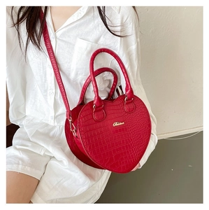 Détail du sac à main cœur rouge avec texture crocodile et logo doré sur robe blanche