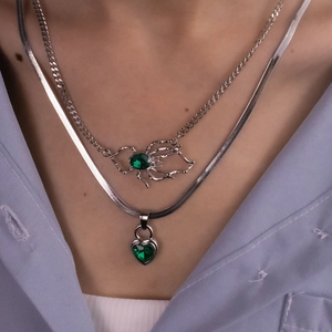 Detail of layered silver necklaces with green heart and spider pendants on lilac shirt