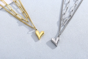 Détail de colliers superposés en or et argent avec maillons carrés et pendentif en cœur