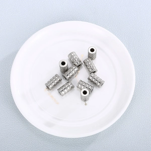 Gros plan de perles cylindriques creuses en acier inoxydable texturé argenté sur porcelaine