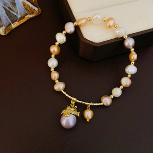 Détail du bracelet en perles d'eau douce avec breloque dorée sur fond en cuir