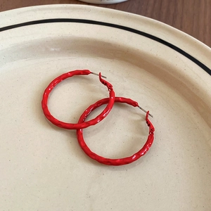 Close-up of red enamel hoop earrings with hammered texture on a beige ceramic plate